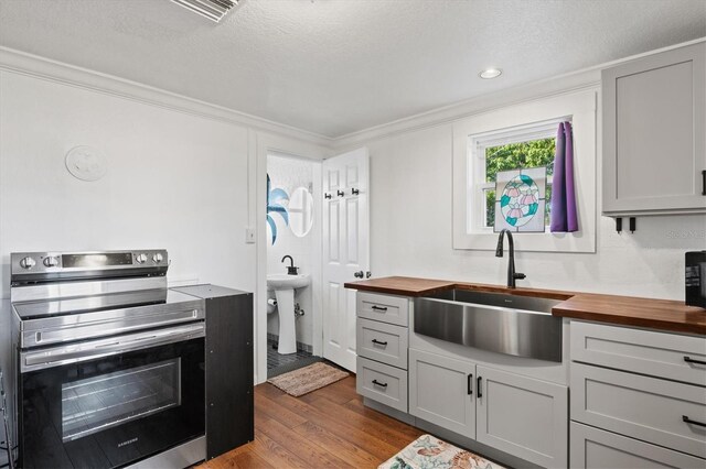 kitchen featuring wood counters, sink, light wood-type flooring, gray cabinetry, and stainless steel electric range