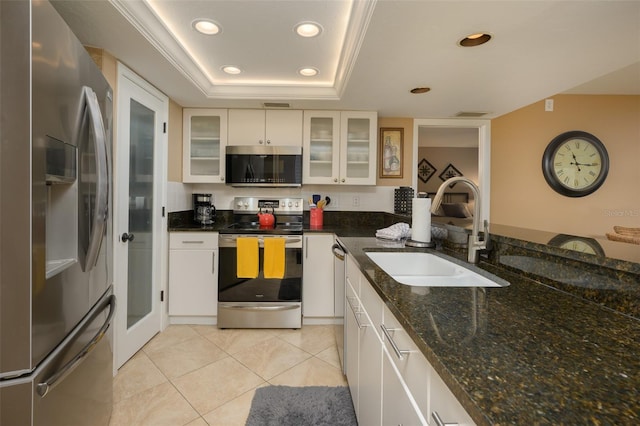 kitchen with dark stone counters, a raised ceiling, sink, appliances with stainless steel finishes, and white cabinetry