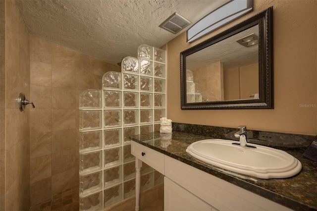 bathroom with tiled shower, a textured ceiling, and vanity