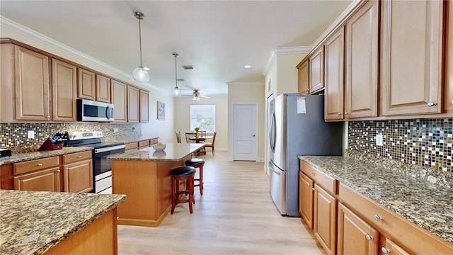 kitchen featuring a center island, hanging light fixtures, light wood-type flooring, appliances with stainless steel finishes, and backsplash