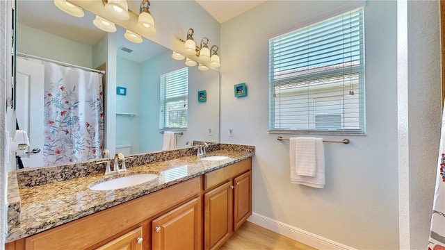 bathroom featuring hardwood / wood-style flooring, toilet, oversized vanity, and dual sinks