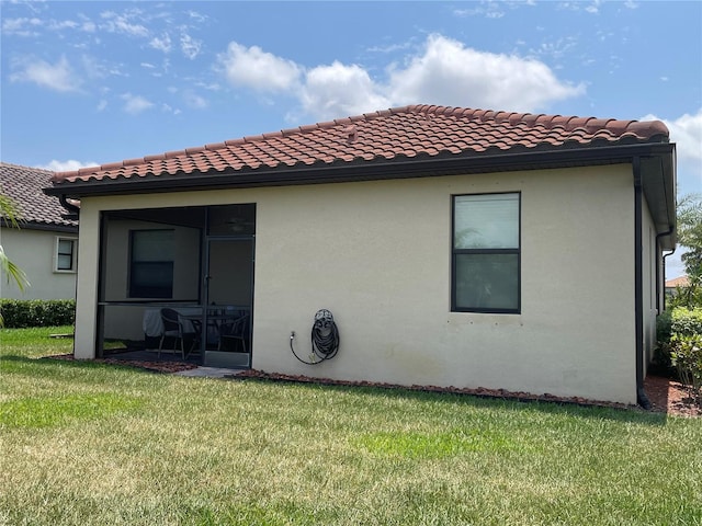 back of property with a tiled roof, a lawn, a sunroom, and stucco siding