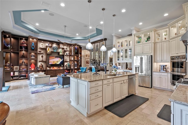 kitchen featuring stainless steel appliances, decorative light fixtures, light stone counters, sink, and a kitchen island with sink