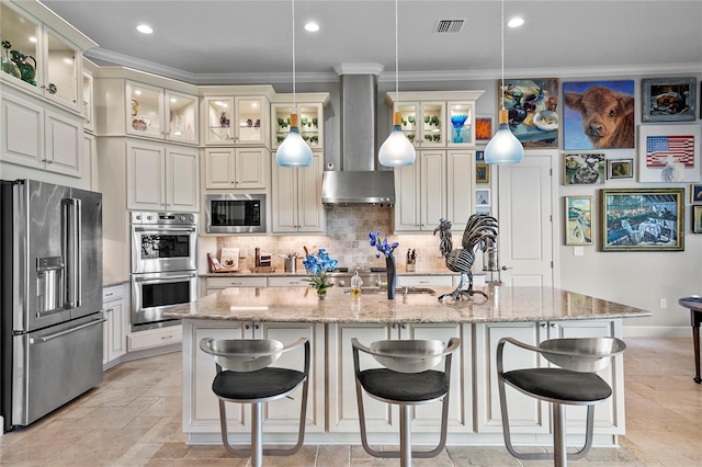 kitchen featuring appliances with stainless steel finishes, wall chimney range hood, light tile floors, and an island with sink