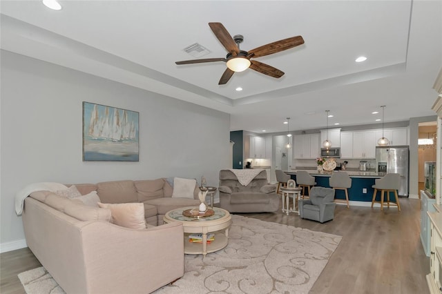 living room featuring a raised ceiling, ceiling fan, and light wood-type flooring