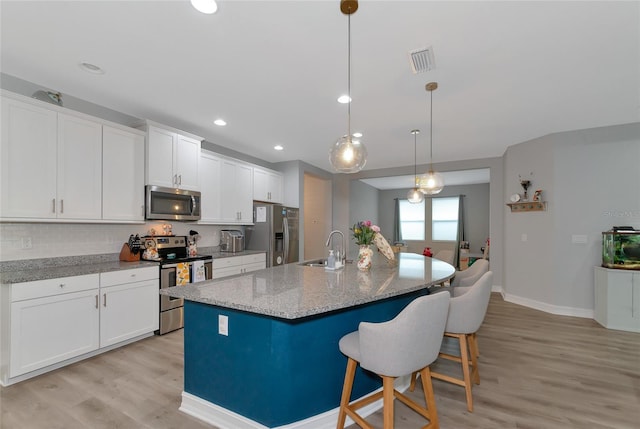 kitchen featuring stainless steel appliances, light stone counters, decorative light fixtures, a kitchen island with sink, and light wood-type flooring