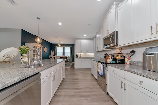 kitchen with light stone counters, stainless steel appliances, sink, decorative light fixtures, and white cabinetry