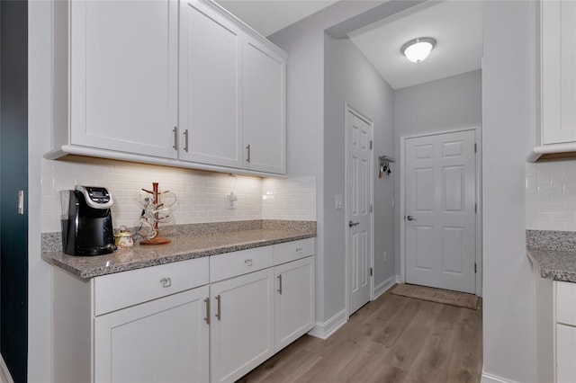 kitchen with decorative backsplash, light hardwood / wood-style flooring, white cabinets, and light stone counters