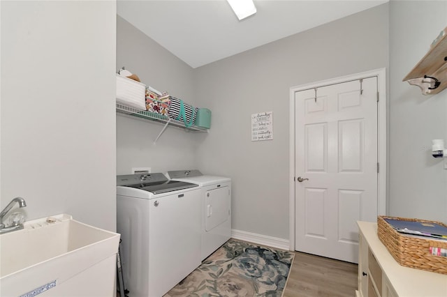 clothes washing area with washer and clothes dryer, light wood-type flooring, and sink