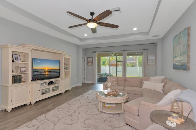 living room featuring hardwood / wood-style flooring, ceiling fan, and a tray ceiling