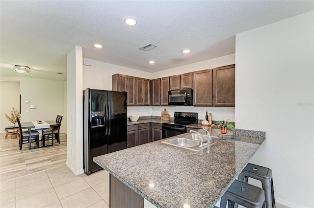 kitchen with sink, kitchen peninsula, a kitchen bar, black appliances, and light wood-type flooring