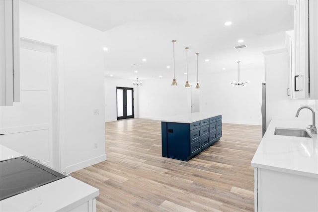 kitchen featuring blue cabinetry, an inviting chandelier, freestanding refrigerator, a kitchen island, and a sink