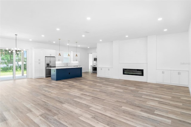 unfurnished living room featuring a sink, light wood-type flooring, a fireplace, a notable chandelier, and recessed lighting