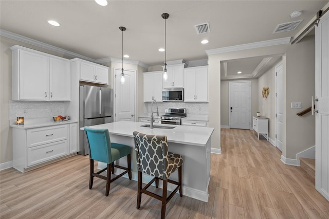 kitchen with hanging light fixtures, a barn door, light hardwood / wood-style floors, white cabinets, and appliances with stainless steel finishes