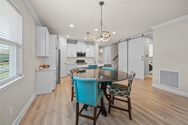 dining room featuring washer / dryer, a barn door, light hardwood / wood-style floors, and crown molding