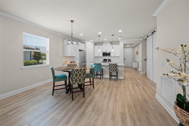 dining space with a barn door, ornamental molding, and light hardwood / wood-style flooring