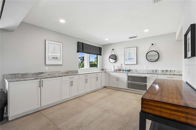 kitchen with sink, white cabinetry, and light stone counters