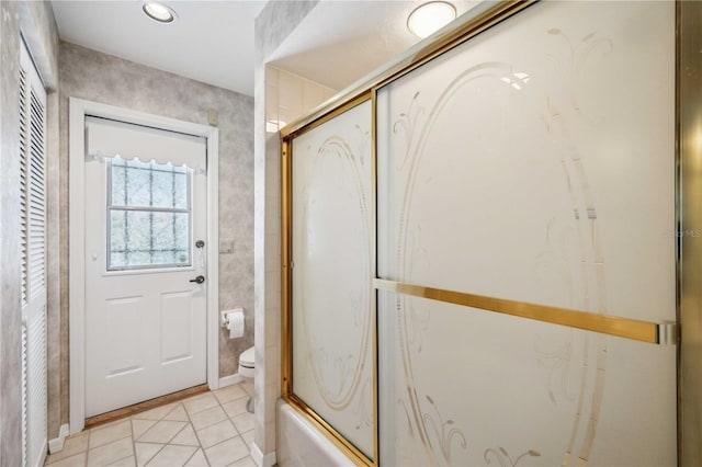 bathroom with tile patterned flooring, bath / shower combo with glass door, and toilet