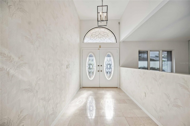 entryway featuring french doors, a towering ceiling, plenty of natural light, and an inviting chandelier