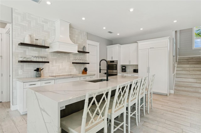 kitchen featuring white cabinets, custom exhaust hood, a spacious island, and sink