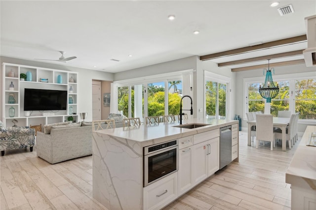 kitchen featuring pendant lighting, a kitchen island with sink, white cabinets, sink, and light stone counters