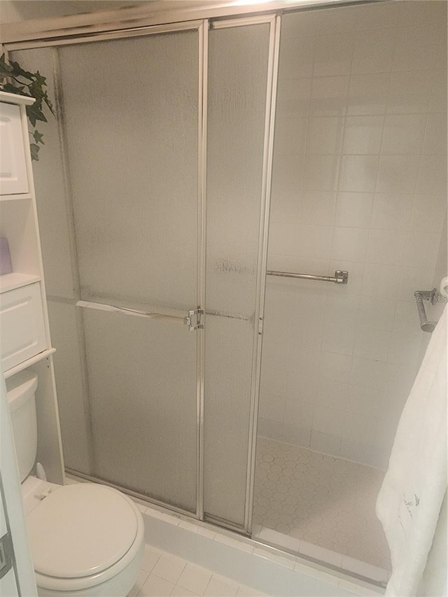 bathroom featuring tile patterned flooring, toilet, and a shower with shower door