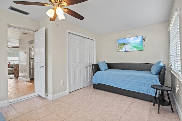 bedroom featuring ceiling fan, a closet, stainless steel refrigerator with ice dispenser, and light tile floors