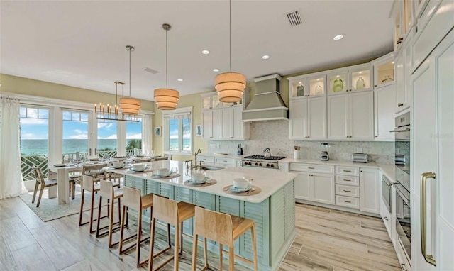 kitchen with a water view, custom range hood, an island with sink, a kitchen bar, and white cabinetry