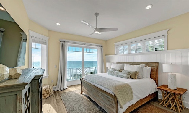 bedroom with access to exterior, a water view, light hardwood / wood-style flooring, and ceiling fan