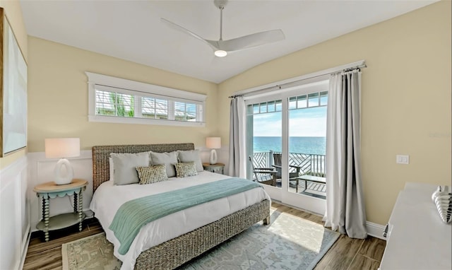 bedroom with access to exterior, ceiling fan, a water view, hardwood / wood-style floors, and lofted ceiling