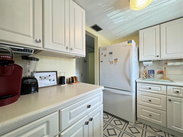 kitchen featuring a textured ceiling, white refrigerator, tasteful backsplash, and white cabinetry