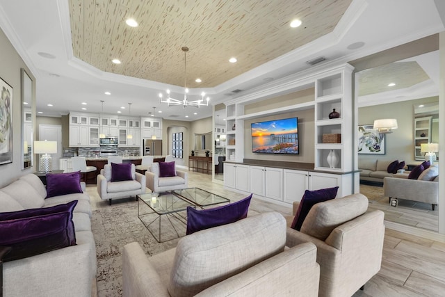 living room with crown molding, built in shelves, light wood-type flooring, a tray ceiling, and a notable chandelier