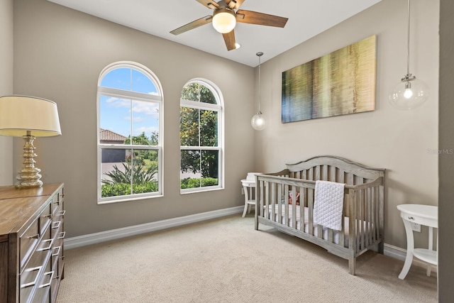 carpeted bedroom with ceiling fan and a nursery area