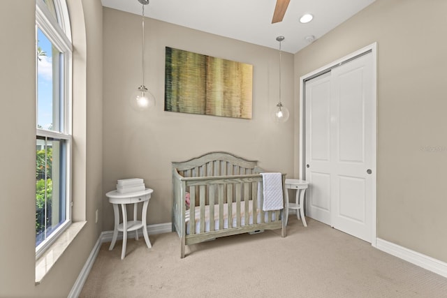 carpeted bedroom featuring ceiling fan, a closet, and a nursery area