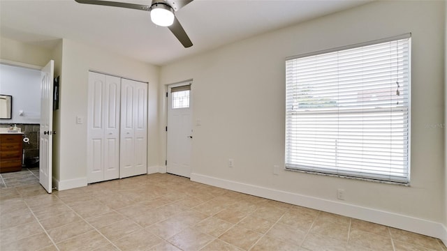 unfurnished bedroom with light tile patterned floors, a closet, ensuite bathroom, ceiling fan, and baseboards