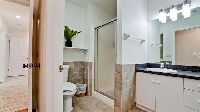 bathroom featuring toilet, a wainscoted wall, vanity, a shower stall, and tile walls