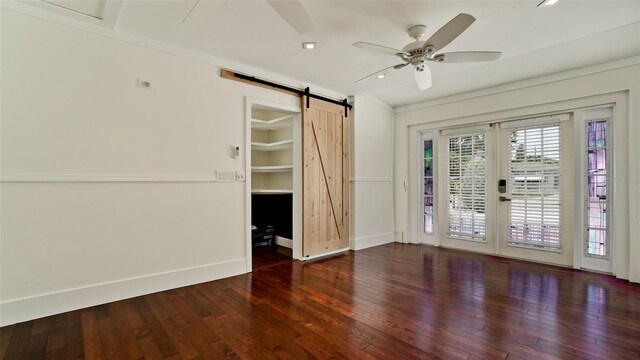 empty room with a barn door, crown molding, ceiling fan, and dark wood-type flooring