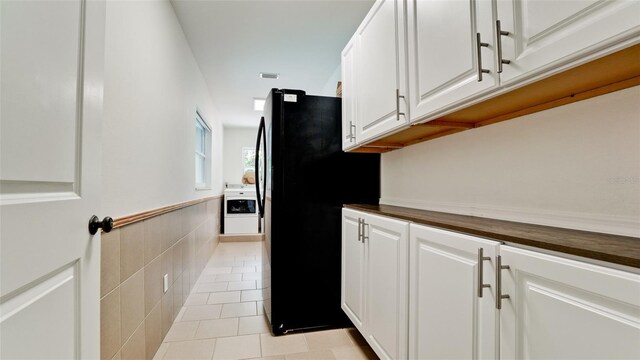 kitchen featuring black refrigerator, light tile patterned floors, tile walls, white cabinets, and butcher block counters