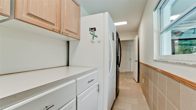 interior space featuring light brown cabinets, tile walls, light countertops, wainscoting, and freestanding refrigerator