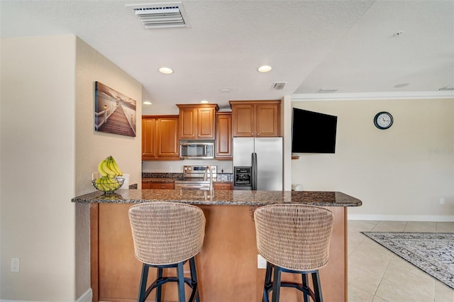 kitchen featuring dark stone countertops, a kitchen bar, stainless steel appliances, and light tile patterned floors