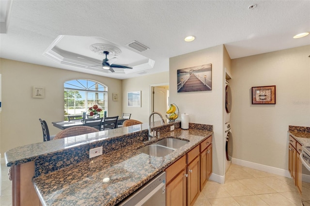 kitchen with ceiling fan, sink, dark stone countertops, a raised ceiling, and light tile patterned floors