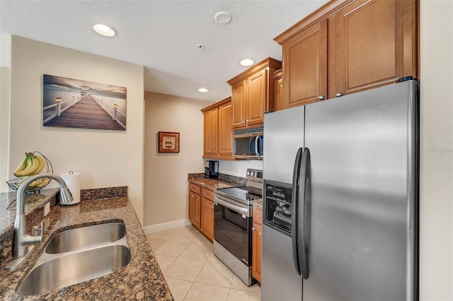 kitchen featuring light tile patterned flooring, stainless steel appliances, sink, dark stone countertops, and a textured ceiling