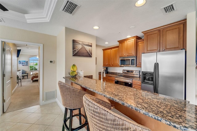 kitchen with dark stone countertops, light colored carpet, appliances with stainless steel finishes, a kitchen breakfast bar, and a raised ceiling