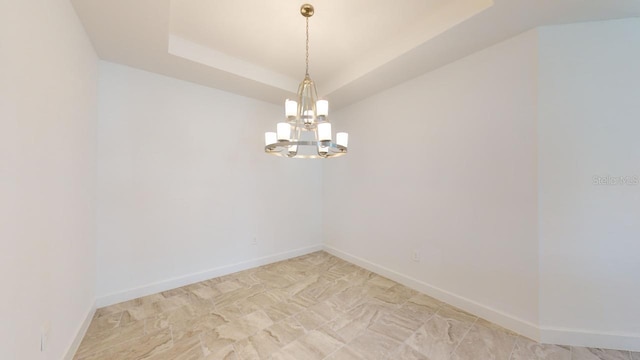 spare room featuring a raised ceiling and a chandelier