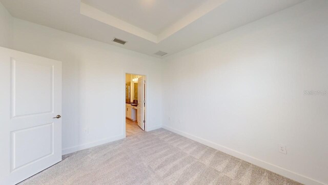 unfurnished room featuring light carpet and a tray ceiling