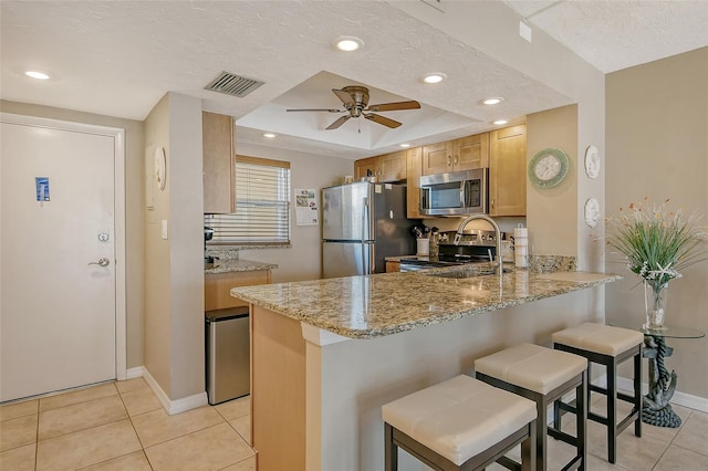 kitchen with visible vents, appliances with stainless steel finishes, a peninsula, light stone countertops, and a kitchen bar