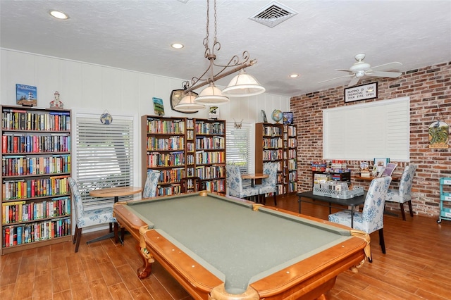 playroom featuring visible vents, a ceiling fan, a textured ceiling, brick wall, and wood finished floors