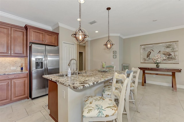 kitchen featuring sink, a kitchen island with sink, stainless steel fridge with ice dispenser, a kitchen bar, and decorative backsplash