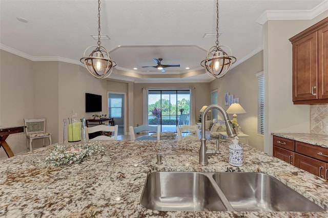 kitchen with tasteful backsplash, light stone counters, ornamental molding, ceiling fan with notable chandelier, and sink