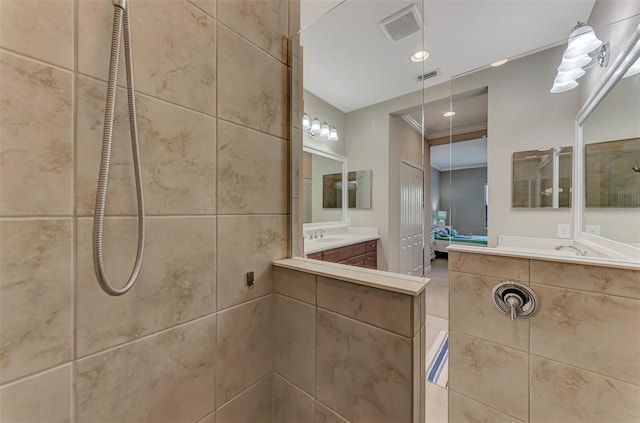 bathroom with a tile shower, vanity, and ornamental molding